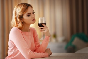 Young woman with glass of red wine on light blurred background